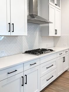 a kitchen with white cabinets and stainless steel stove top oven hood over an island counter