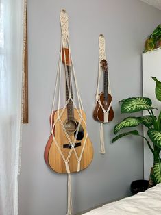 two guitars are hanging on the wall next to a plant