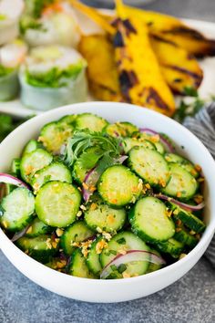 a white bowl filled with cucumbers and onions next to other vegetables on a table