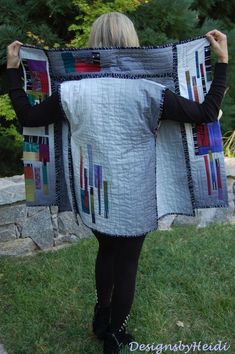 a woman is holding up a quilted blanket in the grass with trees behind her