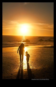 a woman and child walking on the beach at sunset