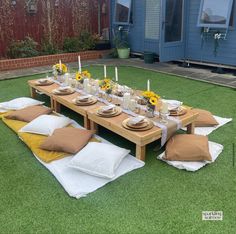 a table set up with pillows and place settings on the grass in front of a blue building