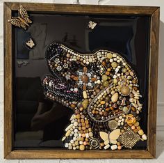 an animal made out of beads and other items in a wooden frame on a white brick wall