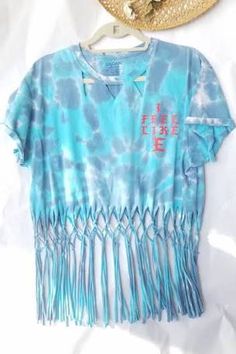 a blue tie dye shirt with fringes hanging on a hanger next to a straw hat