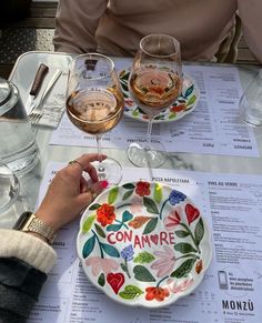 a person holding a wine glass in front of a plate with flowers on it