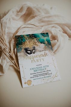 an elegant masquerade party card with feathers on the table next to white fabric