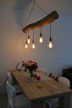 a wooden table topped with white chairs next to a light bulb chandelier hanging from the ceiling