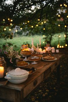 a wooden table topped with plates and bowls filled with food next to lit up candles