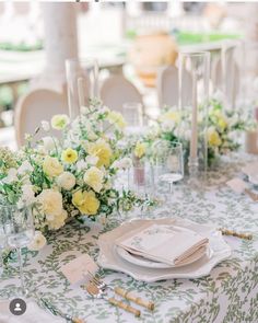 the table is set with white and yellow flowers, napkins, silverware and place settings