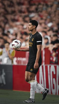 a man holding a soccer ball in his hand while standing on a field with people watching