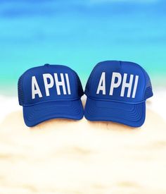 two hats sitting on top of a sandy beach next to the ocean with the word aphi written in white