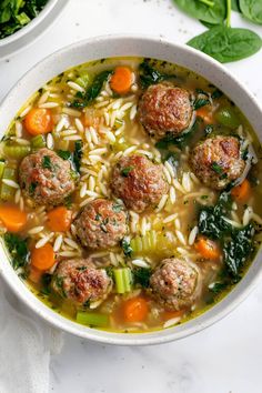 a white bowl filled with meatballs and pasta soup next to a green leafy salad