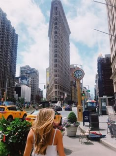 a woman is walking down the street in front of tall buildings and a clock tower