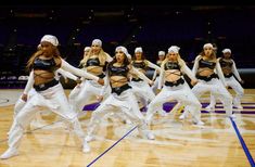 a group of women dancing on top of a basketball court in white pants and black tops