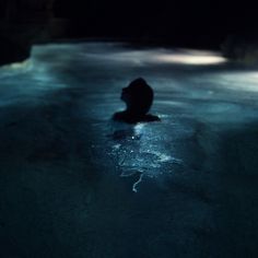 a person sitting in the water at night with their head turned to the side,