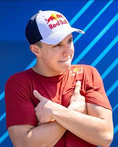 a young man wearing a red bull hat and giving the thumbs up sign in front of a blue wall