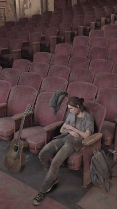 a woman sitting in an empty auditorium with her guitar