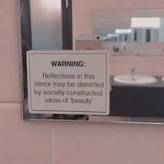 a warning sign is posted on the wall in a bathroom with sinks and mirrors behind it