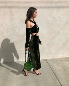 a woman standing in front of a concrete wall wearing a green dress and holding a green purse