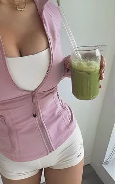 a woman in short shorts holding a glass with a green smoothie on it's side