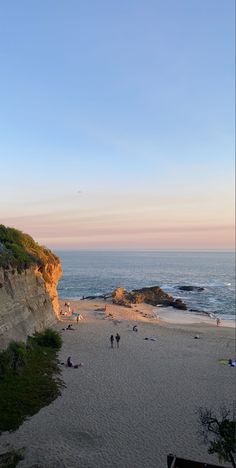 people are walking on the beach by the water at sunset or sunrise, with cliffs in the background