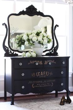 a black dresser with flowers and a mirror on top