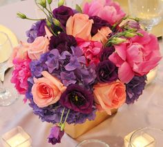 a vase filled with purple and pink flowers on top of a table next to candles