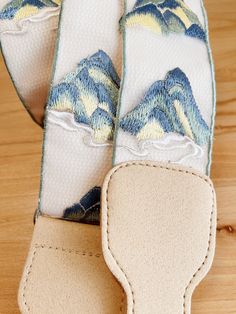 a pair of blue and yellow mountain print guitar straps on a wooden surface with white stitching