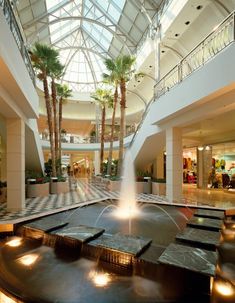 a fountain in the middle of a mall with palm trees and lights on either side