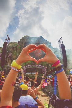 two people making a heart shape with their hands in front of an outdoor concert stage