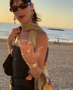 a woman standing on top of a sandy beach holding her hand up in the air