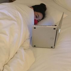 a woman laying in bed with her head on the pillow and looking at an apple laptop