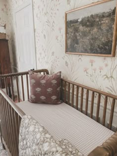 a baby crib with a pillow on top of it in front of a painting