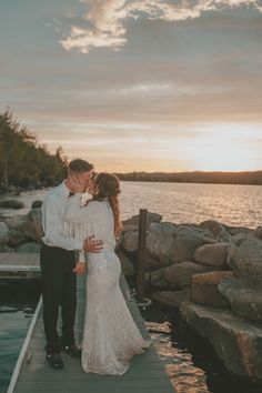 a bride and groom kissing on the dock at sunset