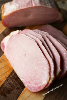 sliced ham sitting on top of a wooden cutting board next to another piece of meat