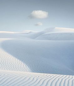 there is a cloud in the sky over some white sand dunes that are covered with snow