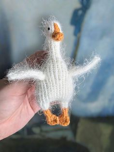 a hand holding a small white knitted duck