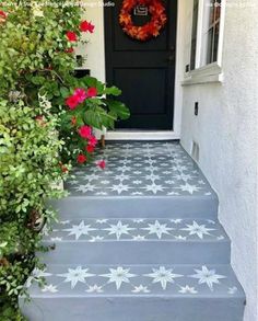 a black door with white stars painted on it and red flowers growing up the steps