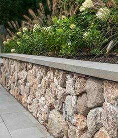 a stone wall with plants and flowers growing out of the top, along side it