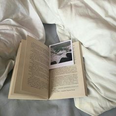 an open book sitting on top of a bed covered in white sheets and pillows,