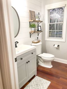 a white toilet sitting next to a sink in a bathroom under a window with wooden floors