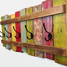 a wooden wall mounted shelf with hooks on the side and colorful wood planks hanging from it's sides