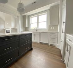 an empty kitchen with white cabinets and wood floors