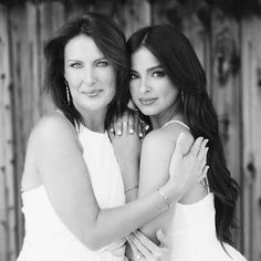 two women hugging each other in front of a wooden fence