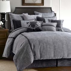 a bed covered in grey and black comforter with pillows on top of the covers