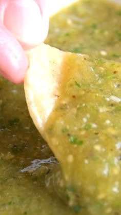 a hand dipping a tortilla into a bowl of soup