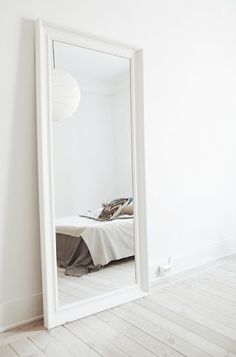 a large white mirror sitting on the side of a wall next to a bed in a room