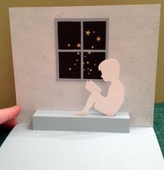 a paper cut out of a person sitting in front of a window reading a book