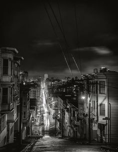 black and white photograph of city street at night with buildings in the foreground, dark clouds overhead