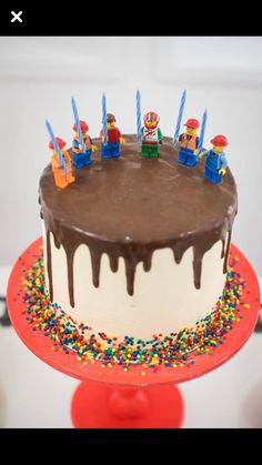 a birthday cake with chocolate icing and sprinkles on top, sitting on a red stand